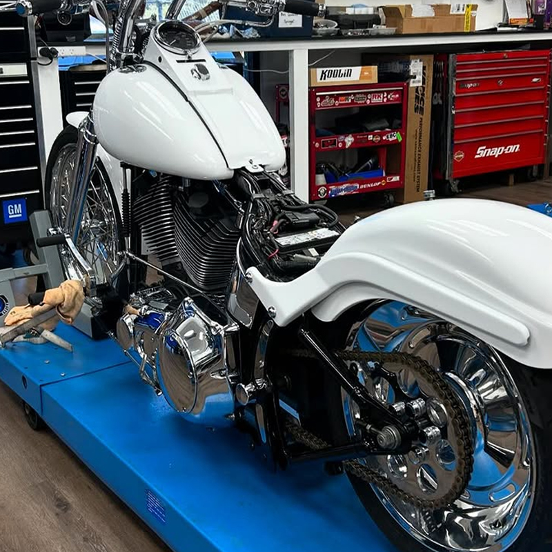 White custom motorcycle with chrome wheels on a blue lift in a workshop