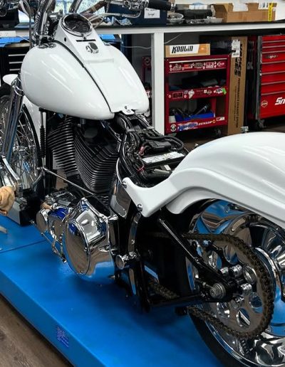 White custom motorcycle with chrome wheels on a blue lift in a workshop