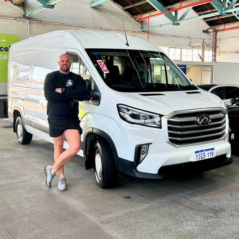 Man with arms folded leaning against a white van in a vehicle workshop